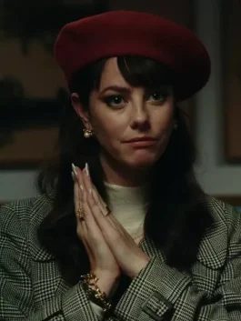 Close-up of Kaya Scodelario in a tartan trench coat and red beret, wearing a luxurious plaid coat with pearl earrings.