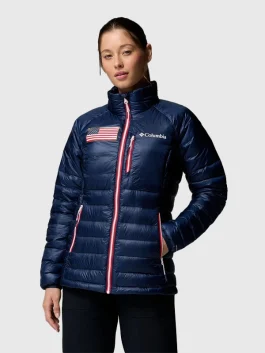 Front view of a woman wearing a navy blue quilted puffer jacket with a US flag patch and white/red zipper accents.