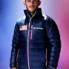 A man wearing a Olympics 2026 Columbia Team USA Puffer Jacket with a US flag patch, "Columbia" logo, and a matching "USA" baseball cap.