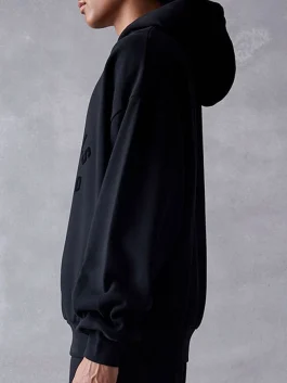 Side view of the Essentials Jet Black Hoodie showing the relaxed drape and hood shape.