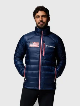 Front view of a man in a navy blue Columbia puffer jacket featuring a US flag on the chest and a high insulated collar.