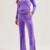 Front view of a purple velour Juicy Couture tracksuit, featuring a zip-up hoodie and matching flared pants with a vertical "Juicy" rhinestone logo on the leg.