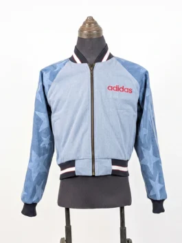 Full front view of the zip-up Adidas Denim Graphic Varsity Bomber Jacket with a light wash torso, star-patterned sleeves, and a red brand logo.