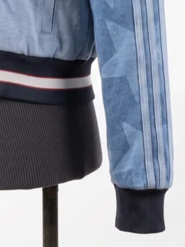 Close-up view of the ribbed knit waistband and matching cuff of the Adidas Denim Graphic Varsity Bomber Jacket, showcasing faded star patterns and stitched stripes.