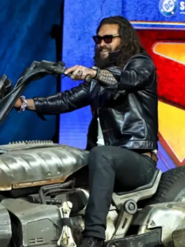 A man with long hair and sunglasses in a polished leather jacket at a red carpet event.