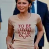 Zendaya wearing a graphic t-shirt with the quote "To Be Loved Is To Be Known" on set.