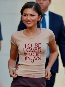 Zendaya wearing a graphic t-shirt with the quote "To Be Loved Is To Be Known" on set.