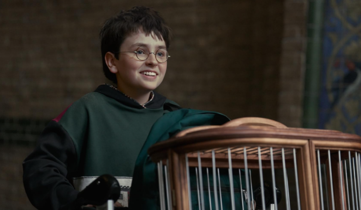 Dominic McLaughlin as Harry Potter in the 2026 HBO TV series wearing Hogwarts robes and holding Hedwig's cage