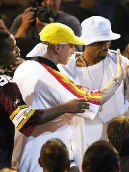 Side profile of Eminem wearing the iconic PnB Nation white track jacket with orange and yellow sleeve stripes and a yellow cap.