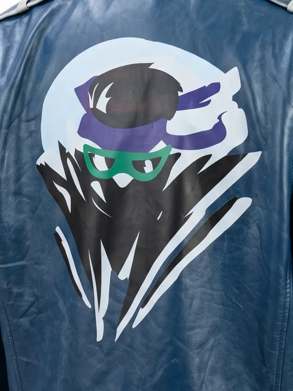 Close-up of the back graphic on the Mortal Kombat 2 Johnny Cage blue jacket, featuring a stylized ninja character art design with a purple headband and green glasses.