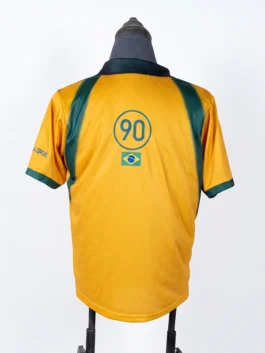 Rear angle of the yellow CJ x Nike Total 90 Retro Brasil Jersey featuring the iconic blue circle 