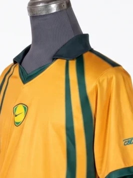 Close-up view of the dark green V-neck polo collar and the centered shield-shaped Nike logo on the front of the yellow CJ x Nike Total 90 Retro Brasil Jersey.