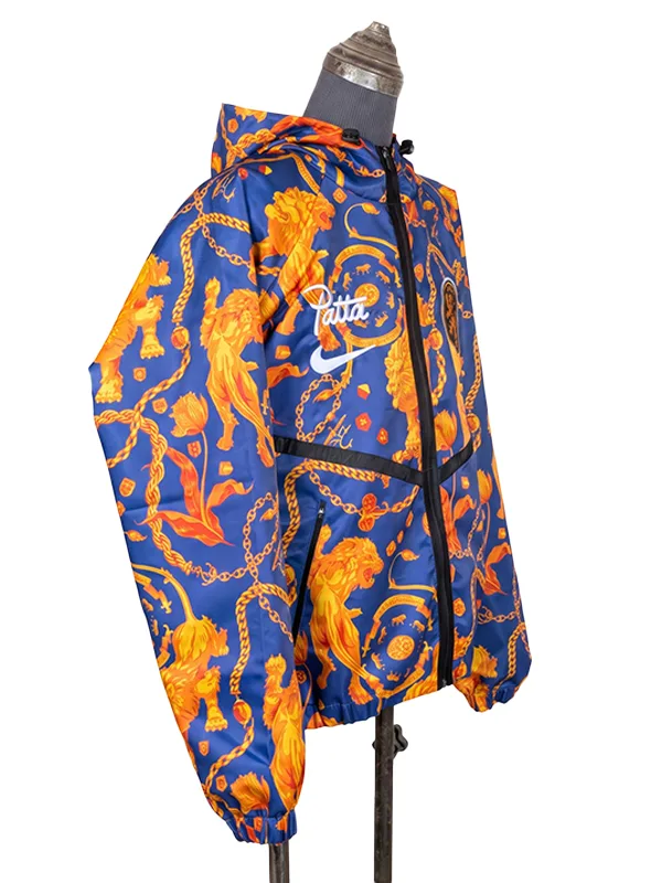 Side profile angle of the vibrant blue and orange Netherlands Anthem Jacket on a retail mannequin, showing the athletic windbreaker build with white Patta and Nike swoosh logos embroidered near the right shoulder line.